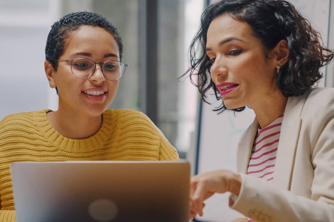 Two women reviewing compliance software on a laptop together.