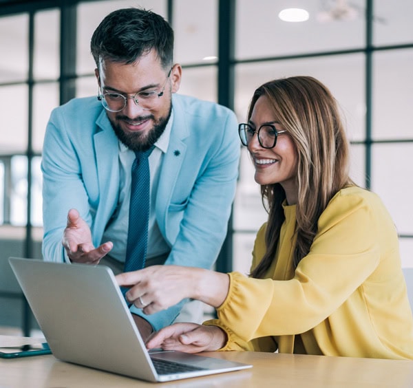 Two professionals smile while working together at a laptop in a modern office.