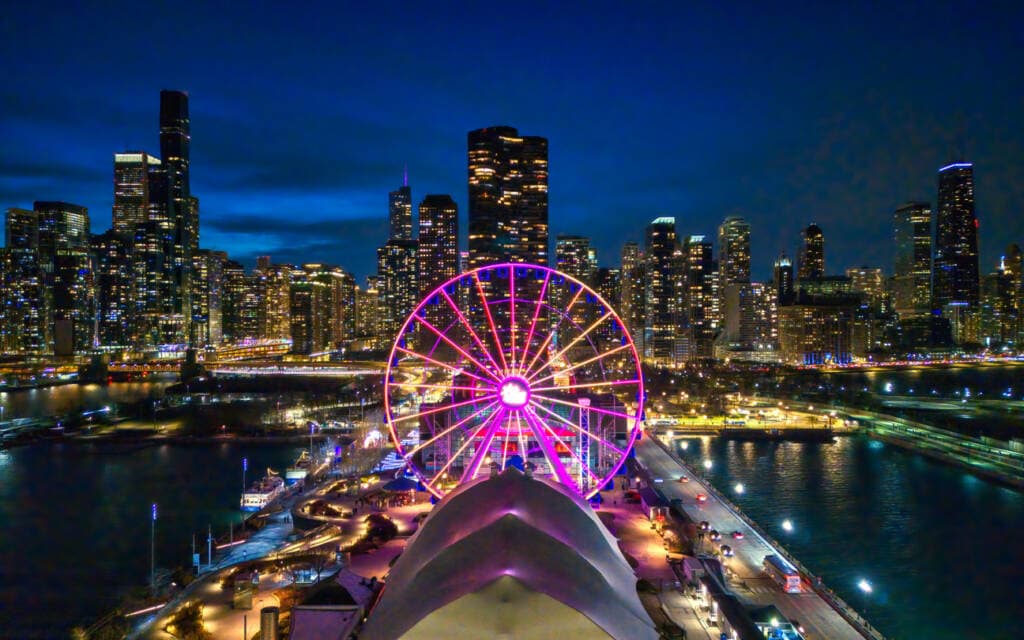 Illuminated Ferris wheel on Chicago's waterfront at dusk with city skyline in background.