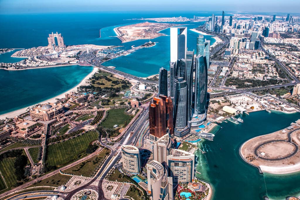 Aerial view of Dubai's waterfront with high-rise towers, artificial islands, and turquoise waters.